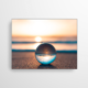 Dieses Akustikbild zeigt den Sonnenuntergang am Strand. In der Glaskugel, welche im Vordergrund im Sand liegt, spiegelt sich dieser traumhafte Anblick.
