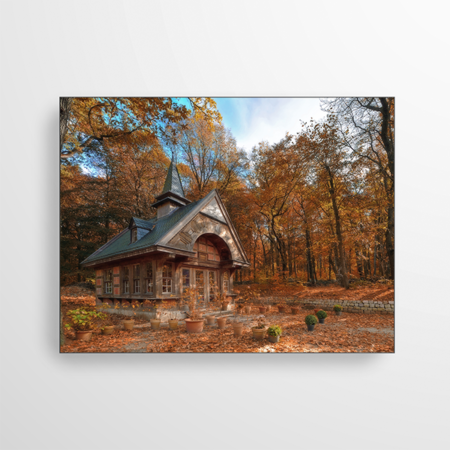 Das Bild zeigt ein Gartenhäuschen inmitten eines braunen Herbstwaldes. Die bunten Blätter passen perfekt zu der hölzernen Kapelle.