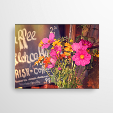 Das Bild zeigt eine Nahaufnahme eines Cafes. Mit Liebe zum Detail wurde der Eingang mit einem Blumenstrauß dekoriert. Im Hintergrund sieht man ein handgeschriebenes Schild, das die Kaffeesorten aufführt.