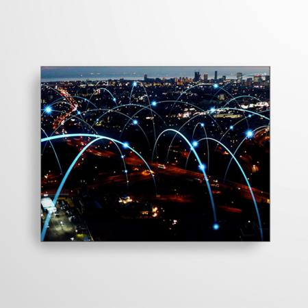 Das Bild zeigt eine Stadt bei Nacht. Über den Dächern sind Licht-Bögen gezeigt, welche verschiedene Standorte miteinander verbinden. Es soll ein Symbol für Netzwerk, Connection, Internet, Industrie und Kommunikation darstellen.