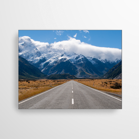 Das Motiv zeigt eine endlos lange Straße, die in die Berge führt. Die beeindruckende Bildlandschaft im Hintergrund wird von weißen Wolken eingebettet.